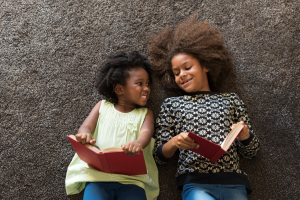 Foto mostra duas crianças negras segurando livros e sorrindo