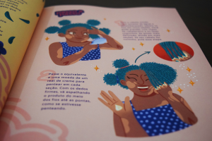 Foto mostra ilustração de menina negra com vitiligo fazendo fitagem no cabelo