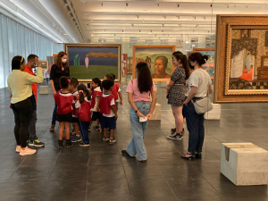 Foto mostra as crianças apresentando a obra Figura Só, de Tarsila do Amaral para os visitantes do museu
