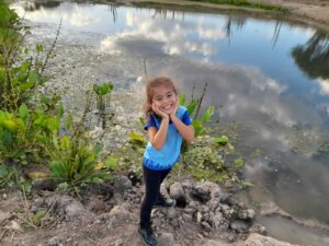 Foto mostra criança sorrindo e, ao fundo, lago com vegetações