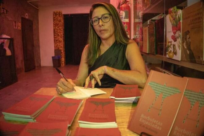 Foto mostra Márcia assinando livro no dia do lançamento de Borboletas Enjauladas