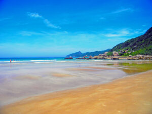 foto de praia deserta, na beira mar com morros ao fundo