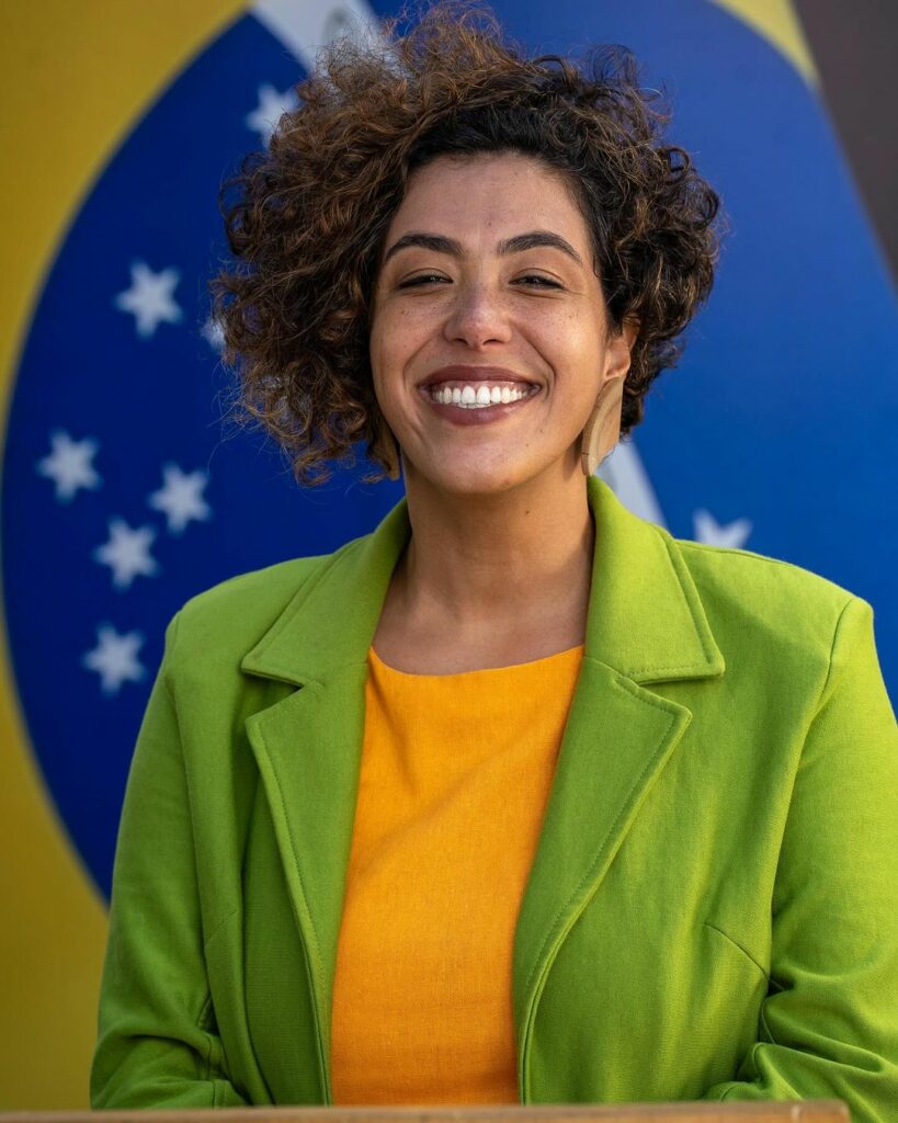 mulher negra de cabelo curto com bandeira do Brasil ao fundo