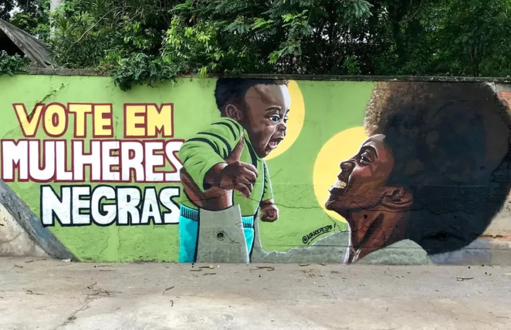 Grafite em que uma mulher negra de black segura um bebê e ao lado os dizeres vote em mulheres negras