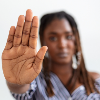 Foto mostra mulher com a mão em sinal de pare, contra a violência doméstica