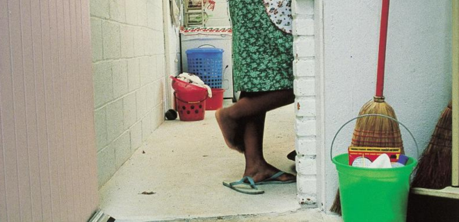 Foto mostra mulher negra de avental lavando louça