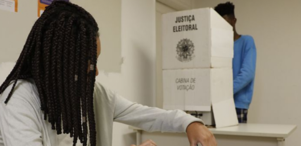 mesária à frente e homem votando em urna eletrônica