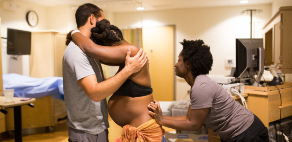 Foto mostra doula dando assistência à mulher em trabalho de parto