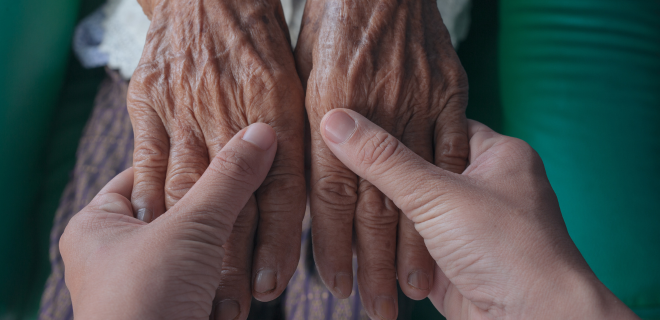 Foto mostra jovem segurando as mãos de idoso, representando a assistência na velhice