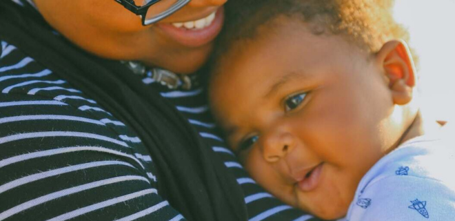 Foto mostra mulher sorrindo segurando crianças. Ambos são negros