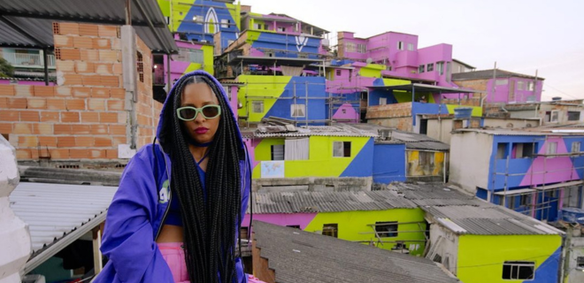 Foto mostra Criola, uma das grafiteiras, e ao fundo, uma favela colorida por ela